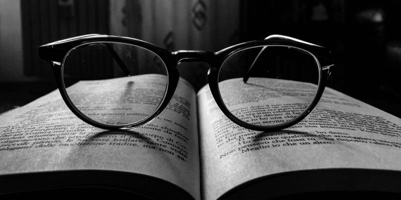 Окуляри лежать на відкритій книзі, сфокусовано на тексті з чорними літерами на італійській мові
