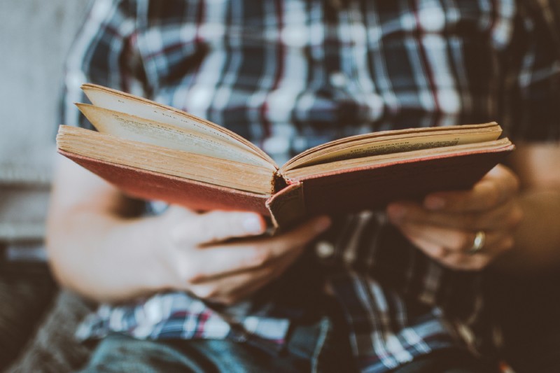 Чоловік у сорочці тримає стару книжку з червоною обкладинкою і читає її