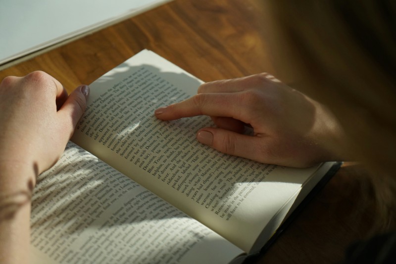 Читач уважно стежить пальцем за рядками тексту у відкритій книжці при денному світлі
